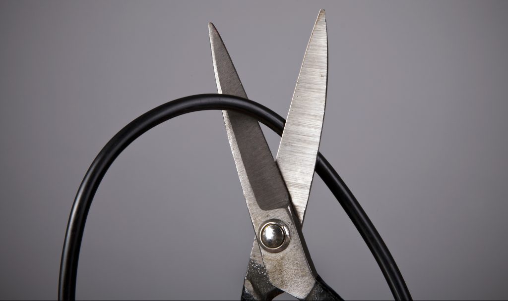 Scissors cutting a computer wire on gray background (wireless or blackout concept)