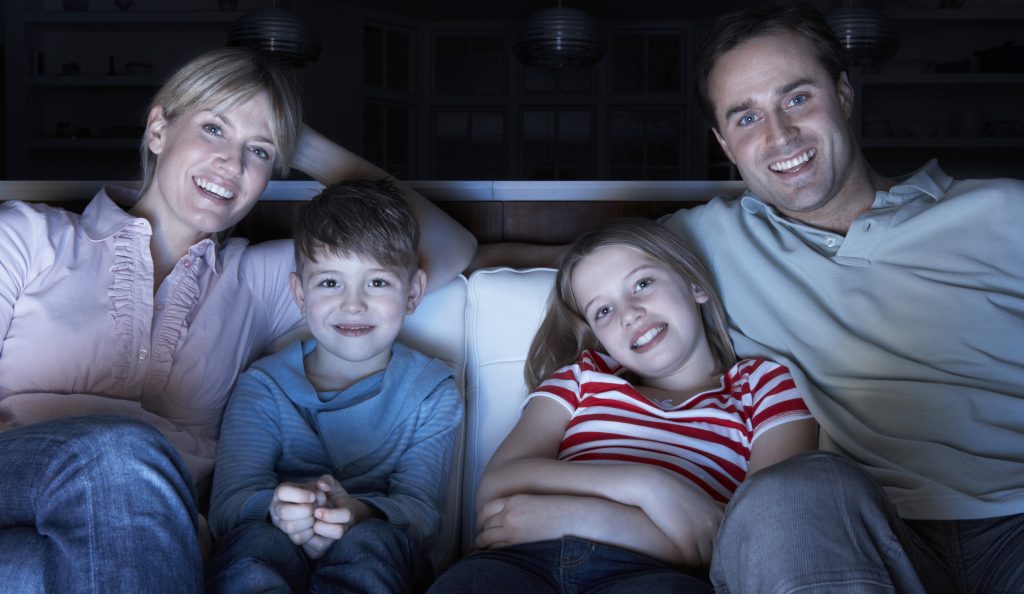 Family Watching TV At Night Sitting On Sofa Together