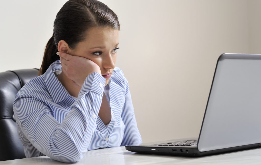 Latin woman looking disappointed at her laptopscreen, sitting behind her desk at the office.