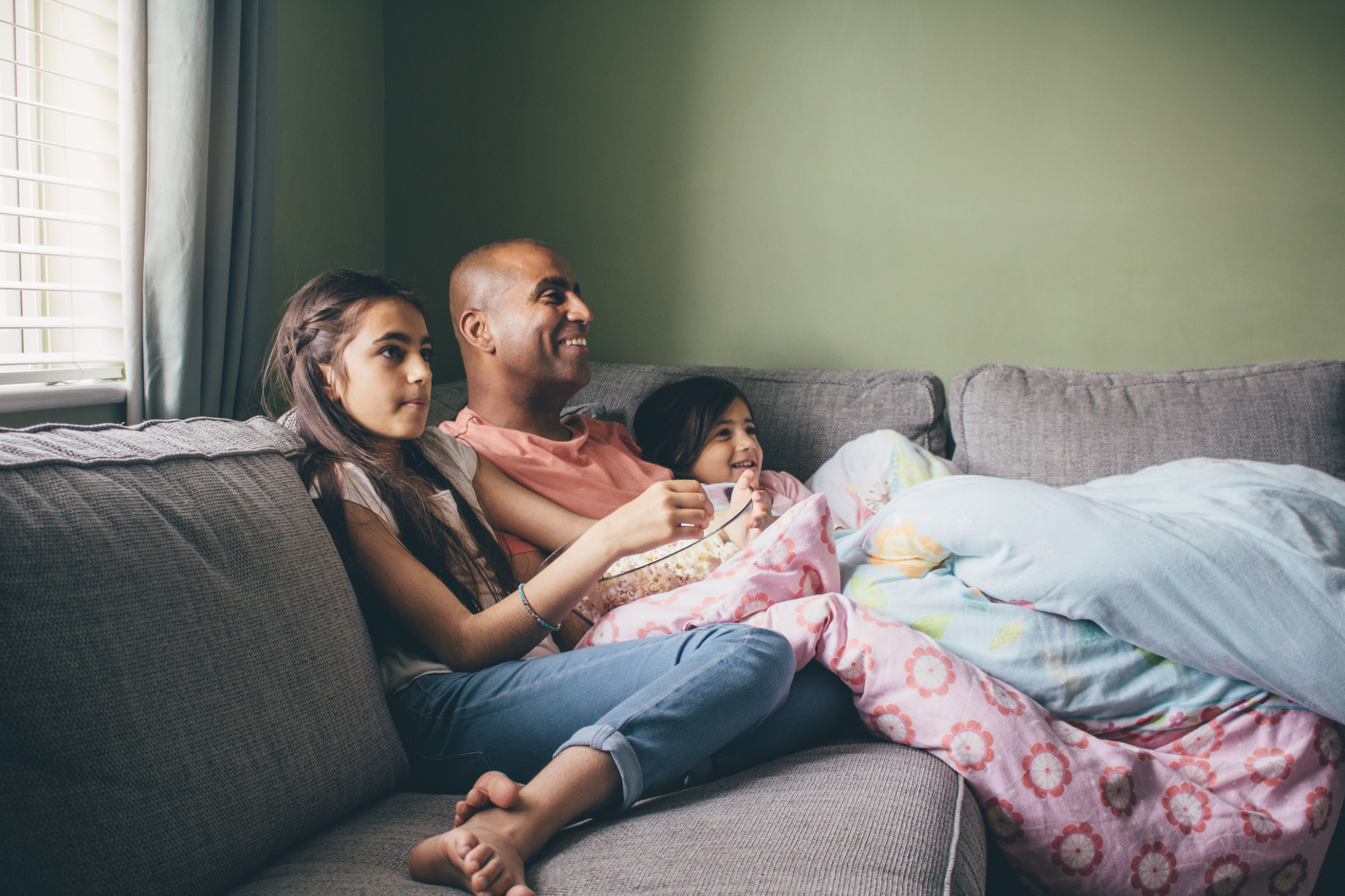 father with two daughters on couch watching tv