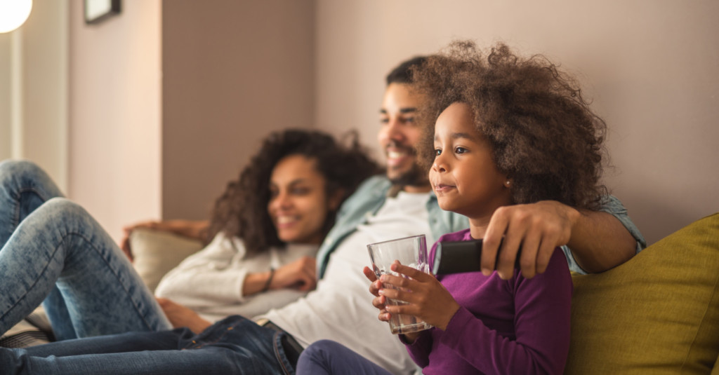 family with little girl sitting on couch watching tv