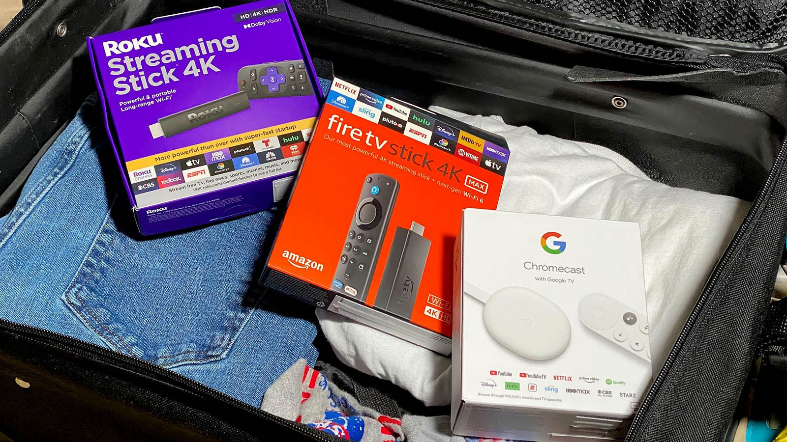 Three streaming devices in a partially packed suitcase.